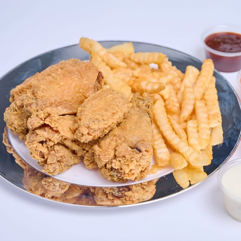 Crispy fried chicken pieces and crinkle-cut fries on a silver platter with dipping sauces.
