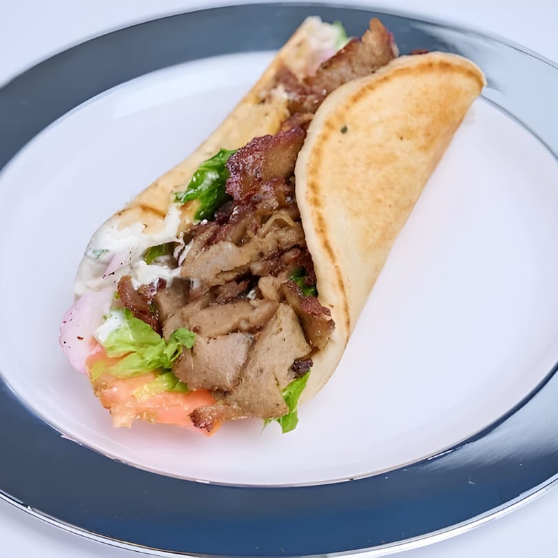 Shawarma Way's delicious shawarma wrap, filled with meat, lettuce, tomatoes, and white sauce, on a white plate.